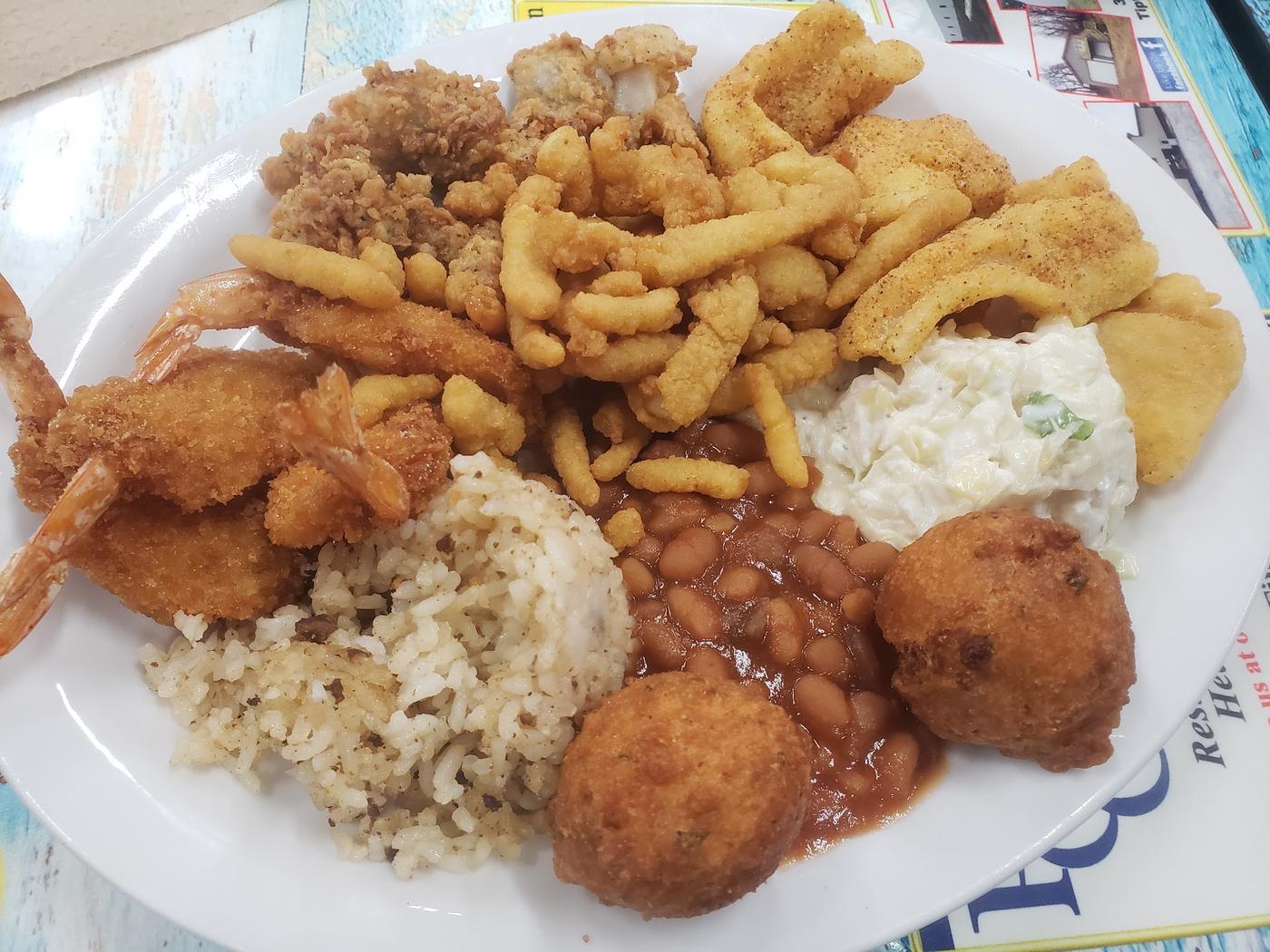 A loaded seafood platter: breaded shrimp, fried fish fillets, clam strips and popcorn shrimp with hush puppies, coleslaw, baked beans and dirty rice.